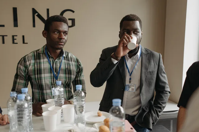 Two businessmen networking at a conference with beverages and name tags. Stellensuche in der Schweiz: Kanäle, Strategien und verdeckter Arbeitsmarkt