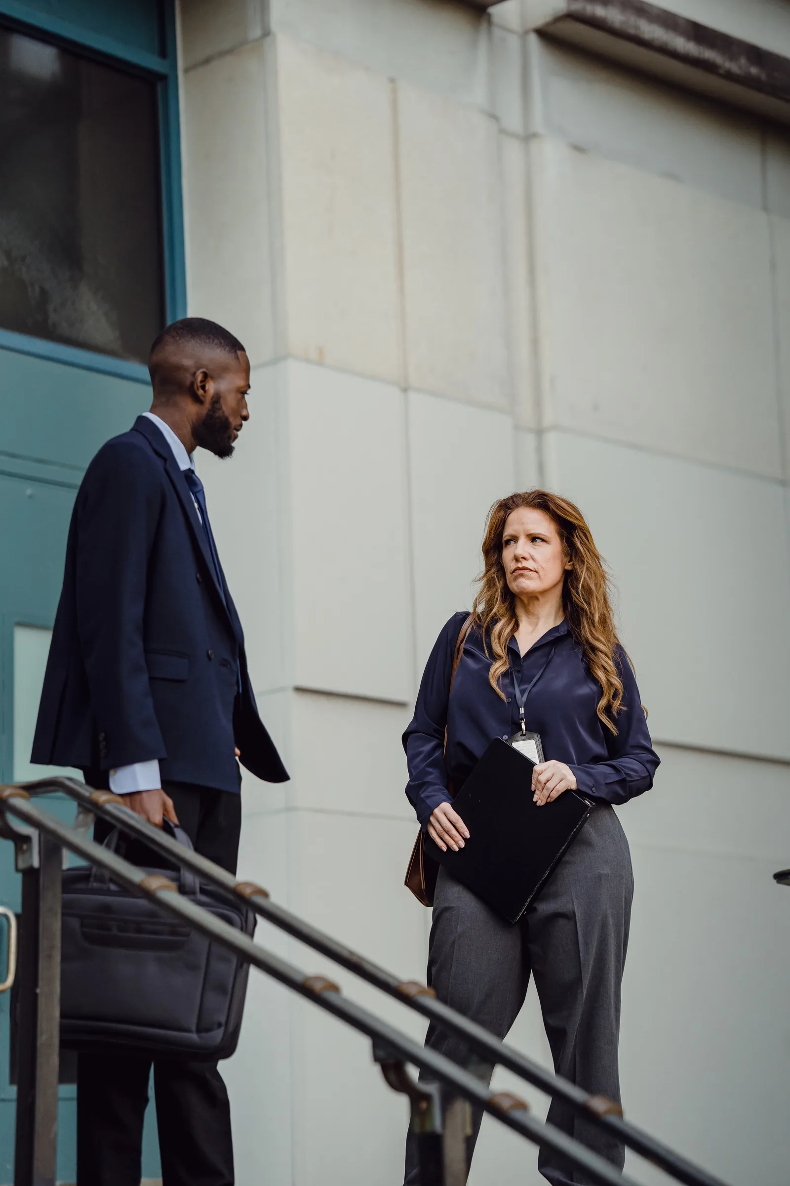 Two professionals in formal attire engage in conversation outside a building.